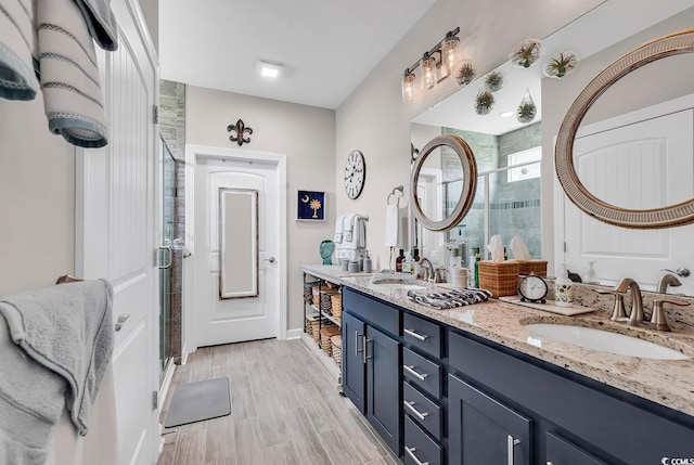 bathroom with wood finished floors, a sink, a shower stall, and double vanity