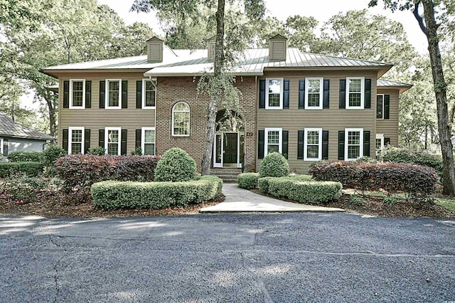 view of front facade with a chimney, a standing seam roof, metal roof, and brick siding