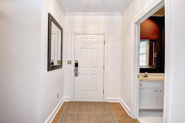 entryway with light wood finished floors, a sink, ornamental molding, and baseboards
