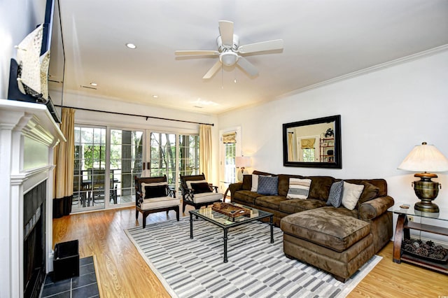 living area featuring crown molding, ceiling fan, wood finished floors, a fireplace, and healthy amount of natural light