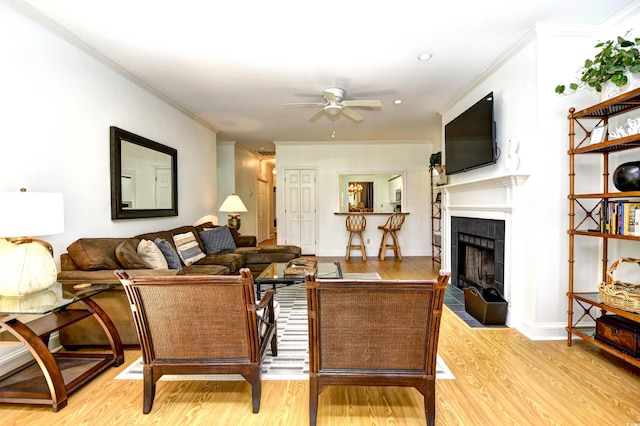 living area with a fireplace, a ceiling fan, ornamental molding, light wood finished floors, and baseboards