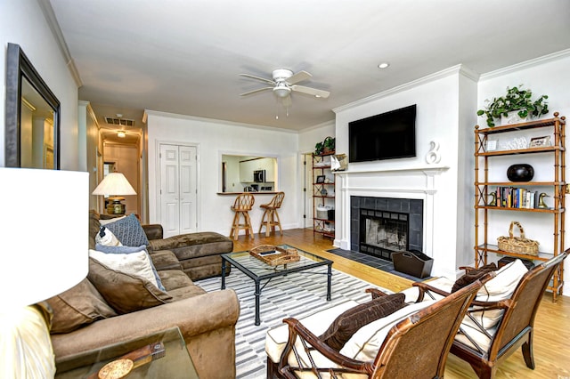 living room featuring ornamental molding, a ceiling fan, wood finished floors, and a tile fireplace