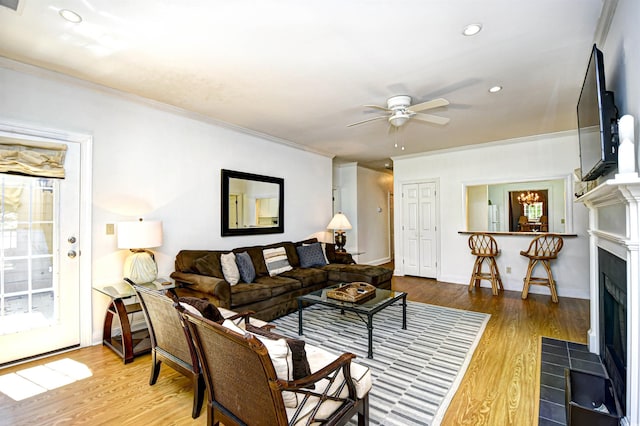 living room featuring a fireplace with flush hearth, ceiling fan, wood finished floors, recessed lighting, and ornamental molding