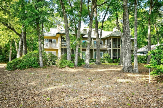 rear view of property featuring a chimney, metal roof, a standing seam roof, and a balcony