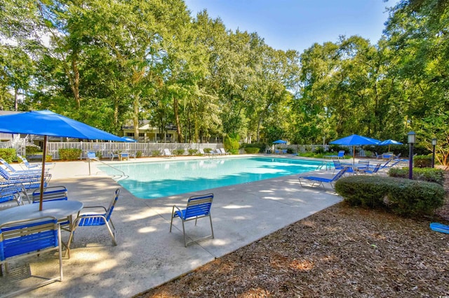 community pool with fence, a patio area, and view of scattered trees