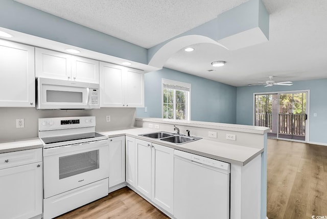 kitchen featuring a peninsula, light wood-style flooring, a sink, white appliances, and light countertops