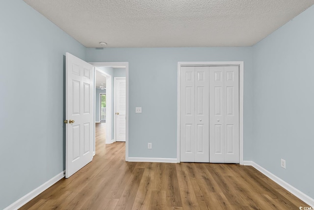 unfurnished bedroom with a textured ceiling, wood finished floors, and baseboards