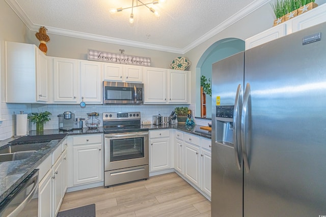kitchen with stainless steel appliances, a textured ceiling, tasteful backsplash, white cabinetry, and ornamental molding