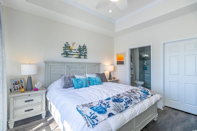 bedroom with dark wood finished floors, a tray ceiling, a ceiling fan, ornamental molding, and connected bathroom