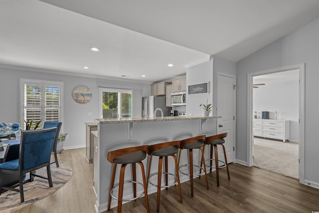 kitchen featuring light wood finished floors, stainless steel appliances, a kitchen breakfast bar, and a healthy amount of sunlight