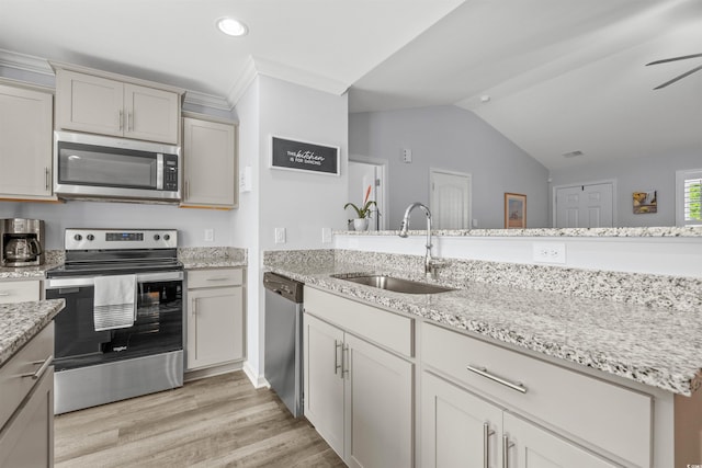 kitchen featuring lofted ceiling, light stone counters, light wood finished floors, a sink, and stainless steel appliances