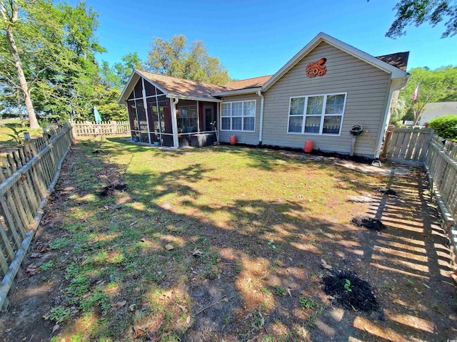 rear view of house with a fenced backyard, a sunroom, and a yard
