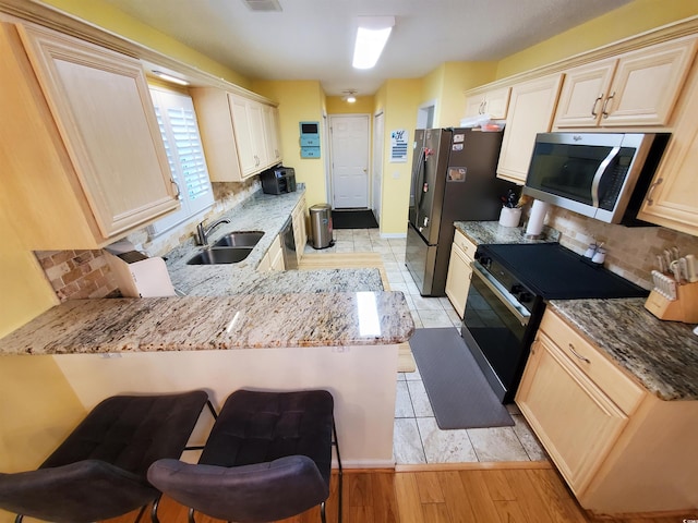 kitchen with stainless steel appliances, a peninsula, a sink, decorative backsplash, and light stone countertops
