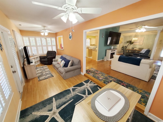 living area with baseboards, a ceiling fan, wood finished floors, and visible vents