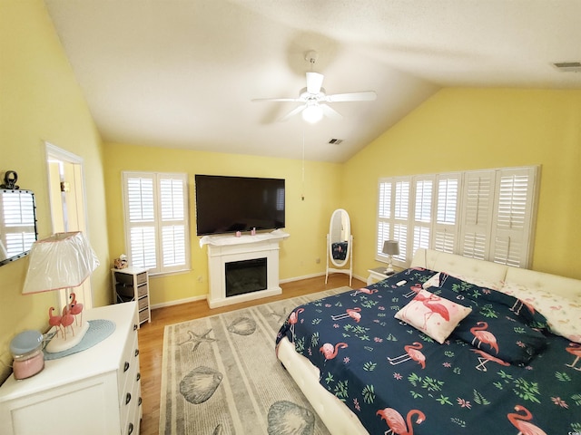 bedroom with lofted ceiling, wood finished floors, visible vents, a ceiling fan, and a fireplace
