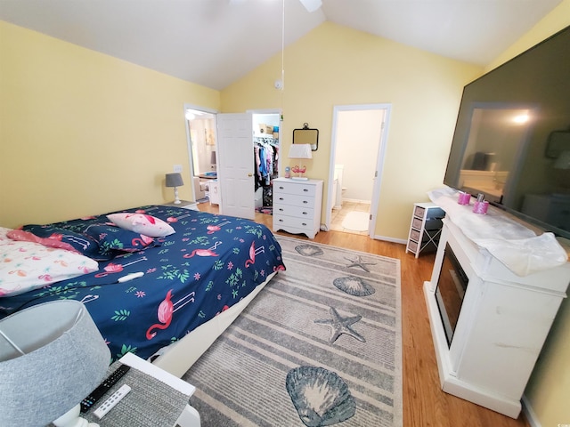 bedroom featuring vaulted ceiling, wood finished floors, ensuite bathroom, a closet, and a walk in closet
