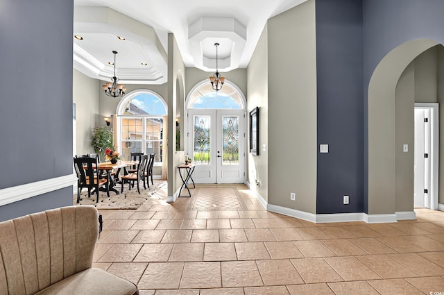 foyer entrance featuring light tile patterned flooring, arched walkways, baseboards, and a tray ceiling