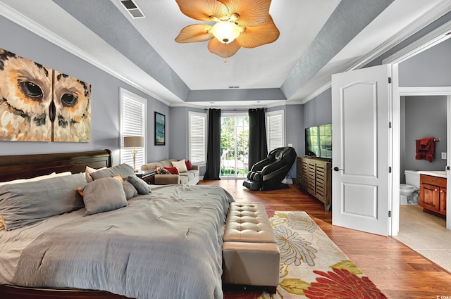 bedroom with connected bathroom, visible vents, a tray ceiling, light wood finished floors, and a ceiling fan