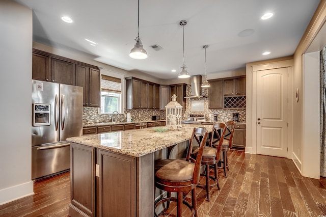 4964 Salt Creek Ct, North Myrtle Beach, SC 29582 - kitchen featuring appliances with stainless steel finishes, wall chimney exhaust hood, a center island, dark wood-type flooring, and light stone countertops