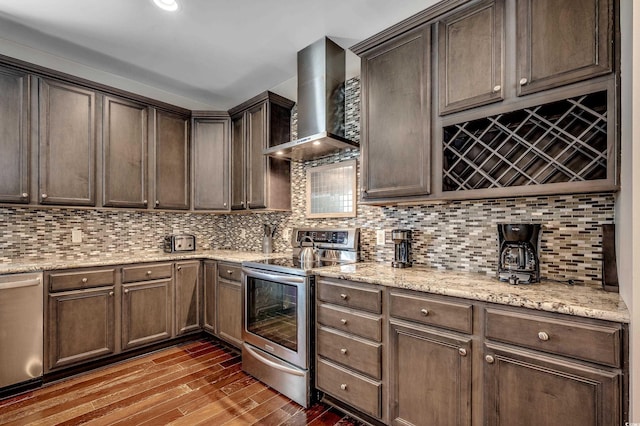 4964 Salt Creek Ct, North Myrtle Beach, SC 29582 - kitchen featuring wall chimney range hood, stainless steel appliances, wood finished floors, decorative backsplash, and light stone countertops