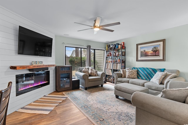 living area with wood finished floors, ceiling fan, and a glass covered fireplace