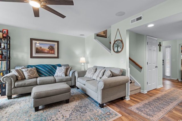 living area with visible vents, wood finished floors, a ceiling fan, and stairway