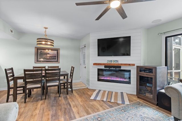 living area featuring a glass covered fireplace, a ceiling fan, visible vents, baseboards, and wood finished floors