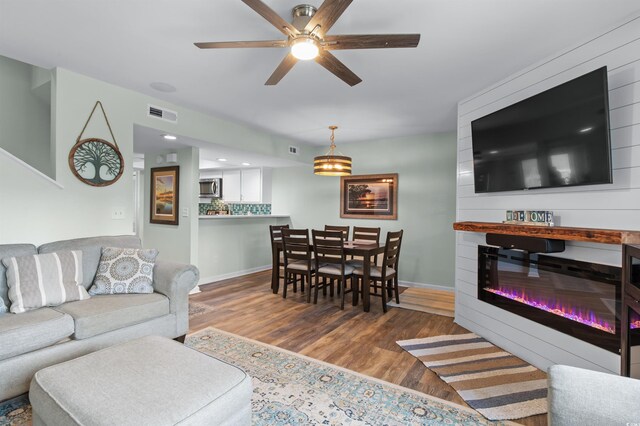 living area with a ceiling fan, visible vents, wood finished floors, and baseboards
