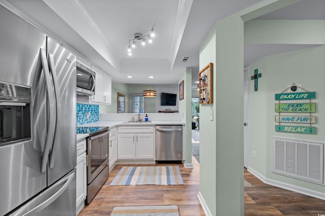kitchen featuring stainless steel appliances, a raised ceiling, visible vents, light wood-style flooring, and ornamental molding