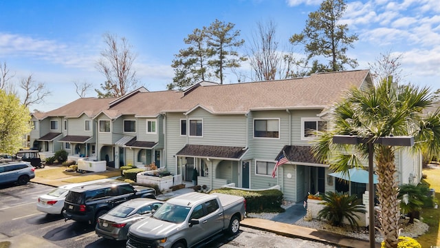 view of front facade featuring roof with shingles, uncovered parking, and a residential view