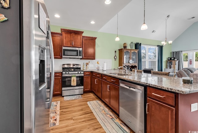 kitchen featuring vaulted ceiling, a sink, light wood finished floors, a peninsula, and appliances with stainless steel finishes