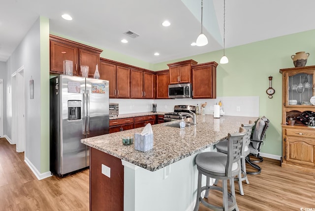 kitchen featuring light wood finished floors, stainless steel appliances, a peninsula, and a kitchen breakfast bar