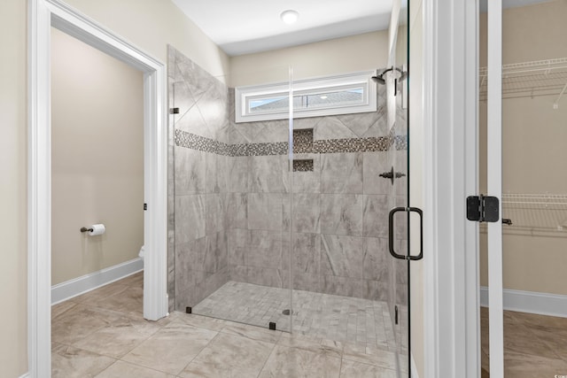 bathroom featuring a shower stall, toilet, a spacious closet, and baseboards