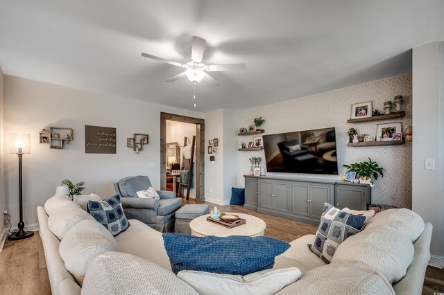 living area featuring a ceiling fan, light wood-style floors, baseboards, and wallpapered walls
