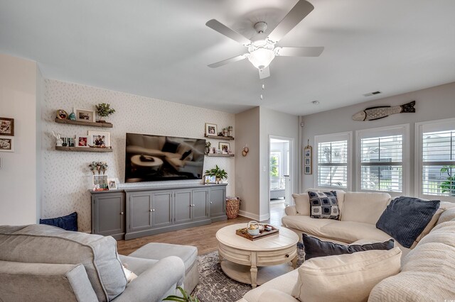 living room with wallpapered walls, healthy amount of natural light, wood finished floors, a ceiling fan, and baseboards