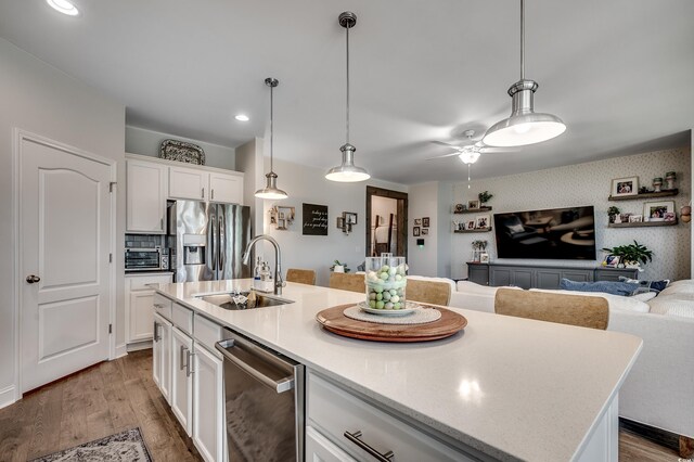 kitchen featuring stainless steel appliances, a sink, wood finished floors, white cabinets, and open floor plan