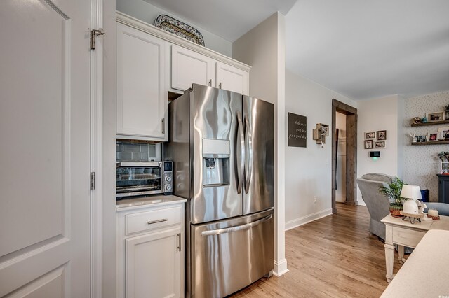 kitchen with stainless steel refrigerator with ice dispenser, light countertops, white cabinets, light wood-style floors, and baseboards