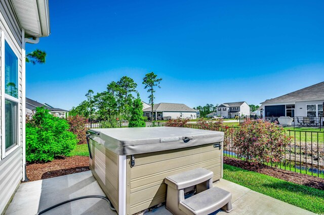 view of patio featuring fence, a hot tub, and a residential view