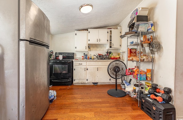 kitchen featuring white cabinets, a textured ceiling, freestanding refrigerator, black electric range oven, and wood finished floors