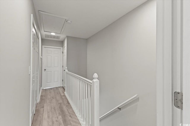 hall with visible vents, an upstairs landing, light wood finished floors, and attic access