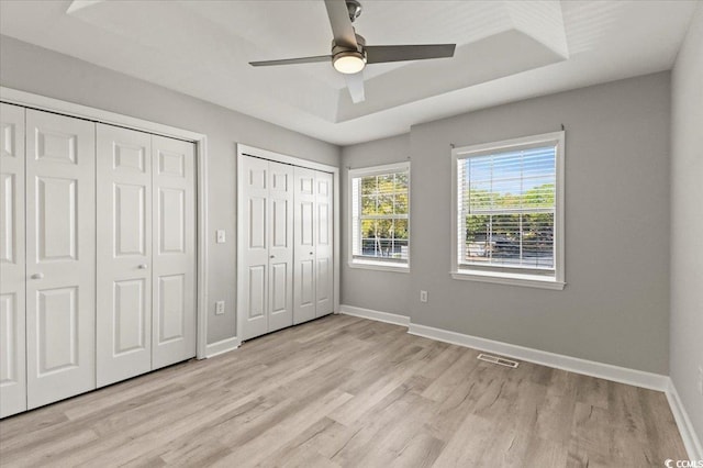 unfurnished bedroom featuring light wood-style floors, multiple closets, a ceiling fan, baseboards, and visible vents