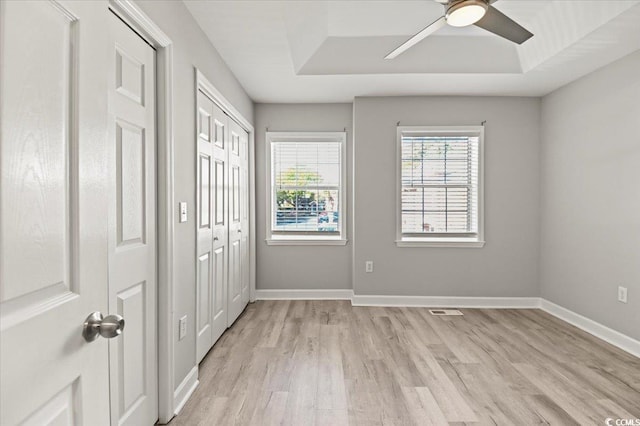 unfurnished bedroom with ceiling fan, visible vents, baseboards, light wood finished floors, and a tray ceiling