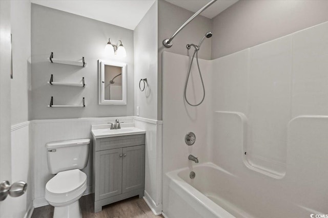 full bath with vanity, wainscoting, wood finished floors, toilet, and shower / bath combination