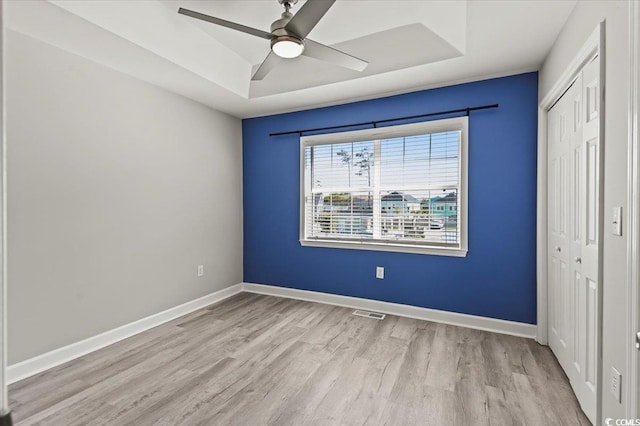 unfurnished bedroom with baseboards, wood finished floors, a raised ceiling, and a closet