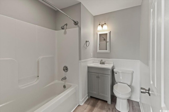 bathroom featuring wainscoting, wood finished floors, vanity, toilet, and tub / shower combination