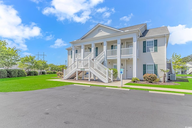 neoclassical / greek revival house featuring covered porch, a front yard, stairs, central AC unit, and a shingled roof