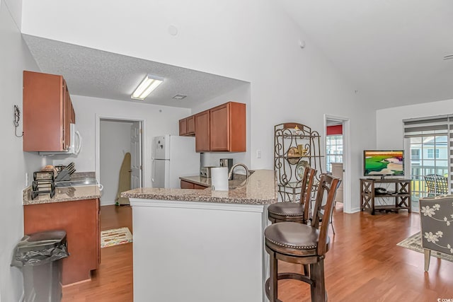 kitchen with brown cabinetry, freestanding refrigerator, a peninsula, light stone countertops, and light wood-type flooring