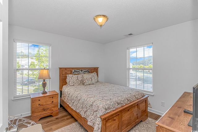 bedroom featuring light wood-style floors, baseboards, multiple windows, and visible vents