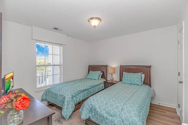 bedroom featuring visible vents, baseboards, a textured ceiling, and wood finished floors