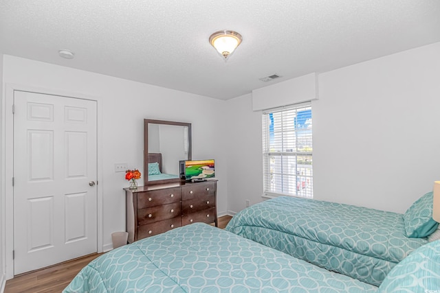 bedroom with a textured ceiling, wood finished floors, and visible vents